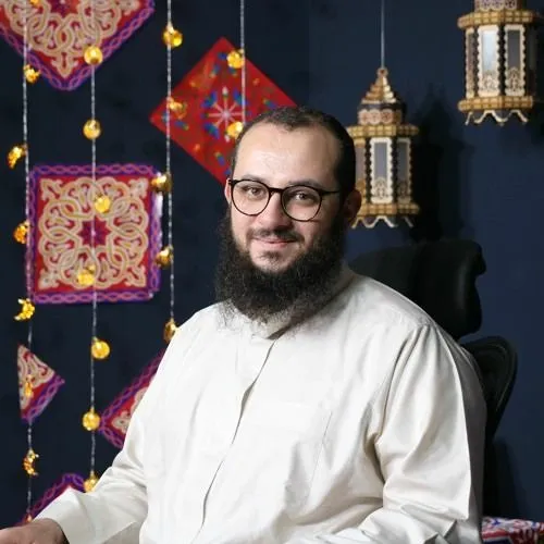 عمرو الشرقاوي مبتسمًا بثوبٍ أبيض أمام فوانيس معلّقة وزخارف ملوّنة