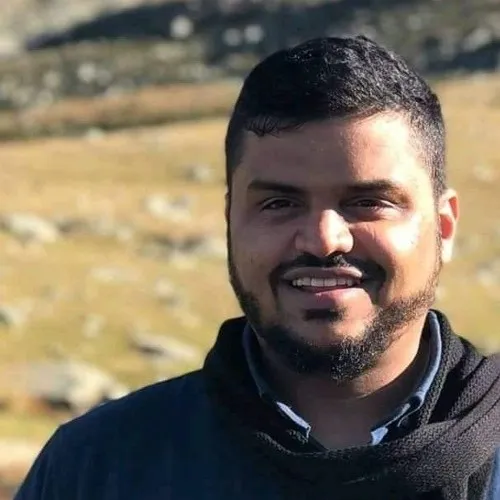 أحمد السيد مبتسمًا في الهواء الطلق أمام سفح جبل