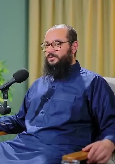عمرو الشرقاوي بثوبٍ أزرق يتحدّث أمام مكبّر صوت في حوارٍ مسجّل