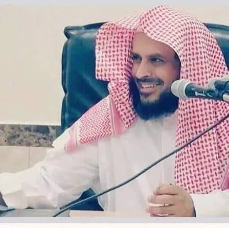 الشيخ عبد العزيز الطريفي مبتسمًا، جالسًا إلى مكتب أمامه مكبّر صوت