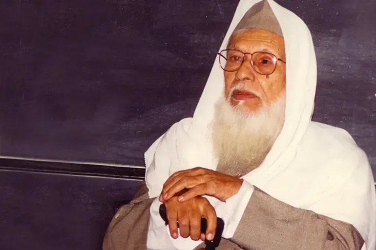 أبو الحسن الندوي متكئًا على عصاه بشالٍ أبيض