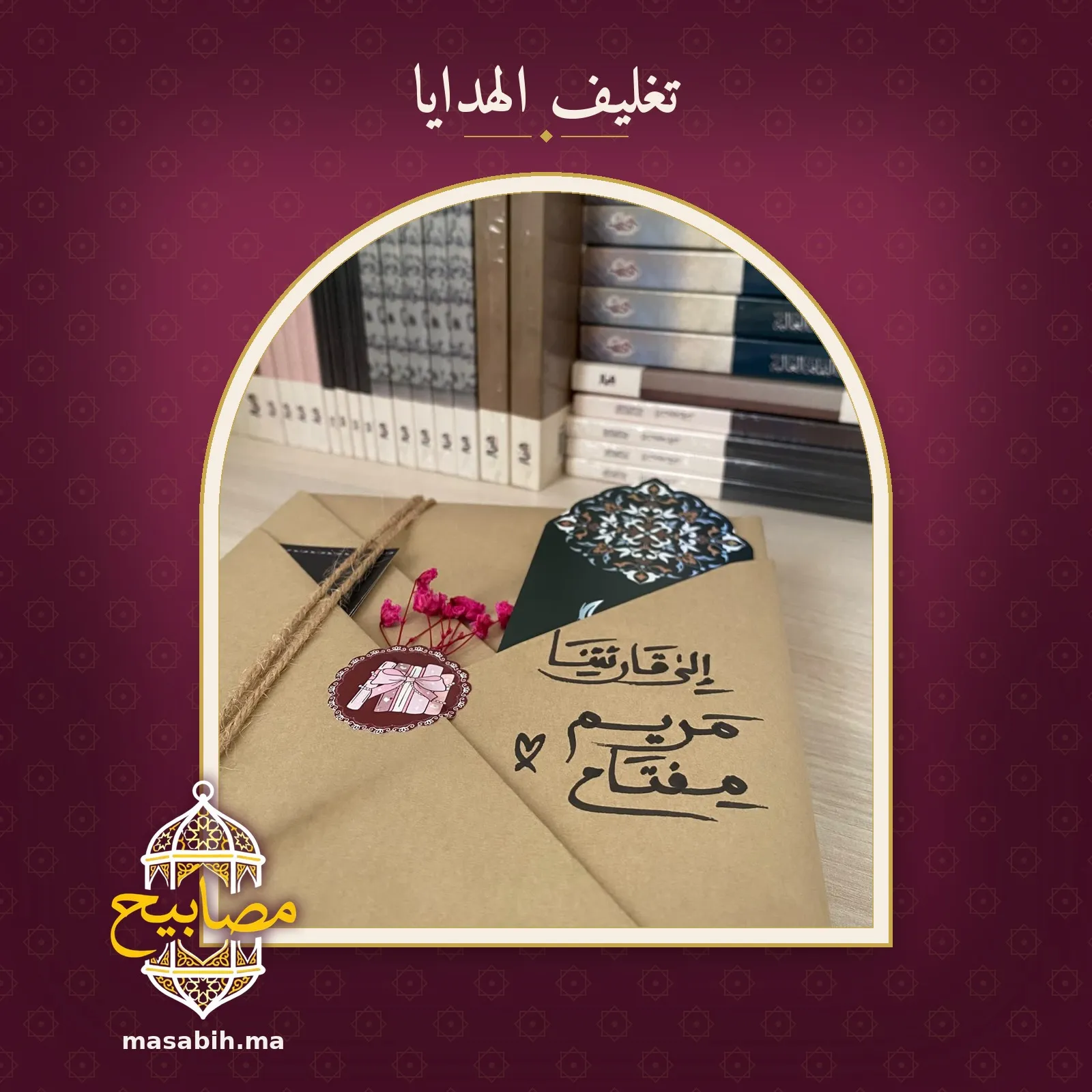 إهداءٌ بخطٍّ عربيٍّ على ورق التغليف، وزهورٌ وردية مجفّفة، وبطاقةٌ بزخرفةٍ هندسية