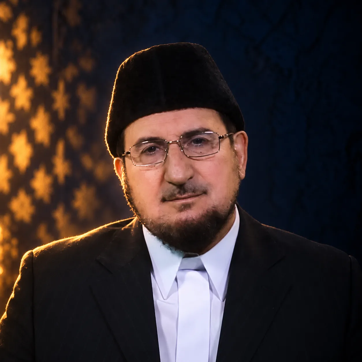 صورة عبد الكريم بكار بلحيةٍ بيضاء ونظارة وطربوش أسود، يرتدي بدلةً داكنة